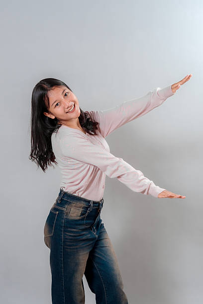 istock Happy young Asian woman smiling brightly while posing playfully with her arms stretched in a fun gesture, conveying joy, friendliness, and a carefree attitude in studio setting. 2245304391