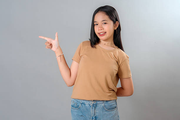 istock A cheerful young Asian woman smiling confidently while pointing to the side with her index finger, expressing excitement, suggestion, or recommendation in a friendly gesture. 2245304616