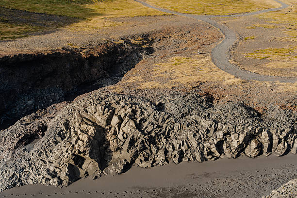 An aerial view showcases a rocky coastline, paths meandering above, and dark sand beaches below, creating a serene coastal landscape.