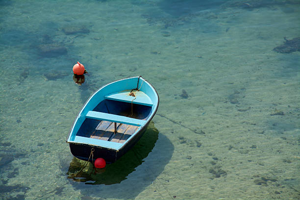 A small blue rowboat floats peacefully in crystal clear turquoise water. The sandy seabed is visible through the calm, transparent water.