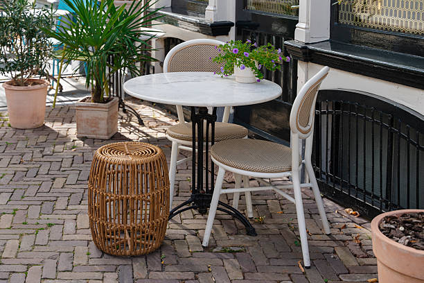 istock Outdoor cafe seating with marble table, chairs, stool, and potted plants on a brick patio. 2245309582