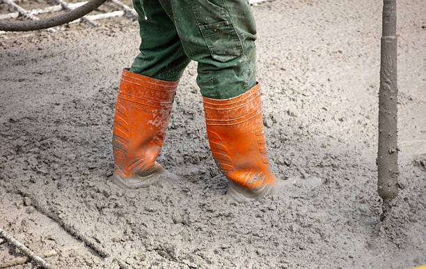 istock Construction worker wearing orange boots standing within wet concrete mix at building site, viewed close-up 2245311696