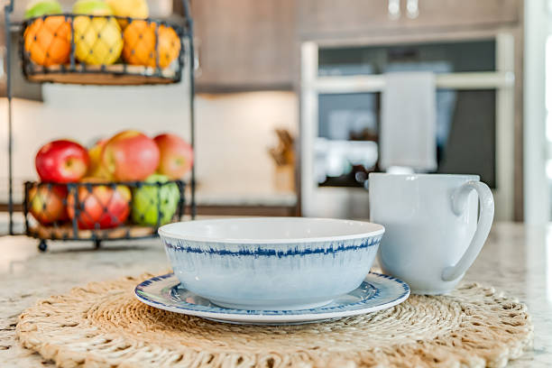 A breakfast setup at a kitchen island, complete with bowl, plate, and coffee mug plus fruit stand in the background
