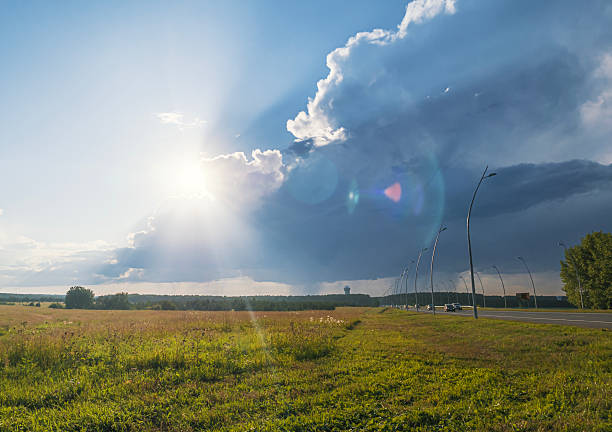 Dramatic cloud formations over a vast grassy field during sunset near a winding road in the countryside.