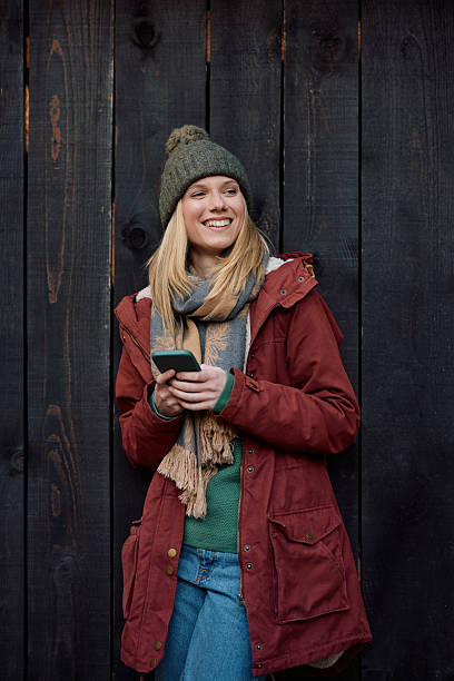 istock Happy woman using cell phone while leaning on wooden wall in autumn. 2245317166