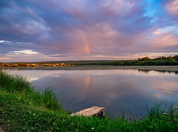 istock Beautiful pink sunset with rainbow reflection over calm lake at countryside evening. Tranquil lake with a wooden dock in the foreground. 2245318733