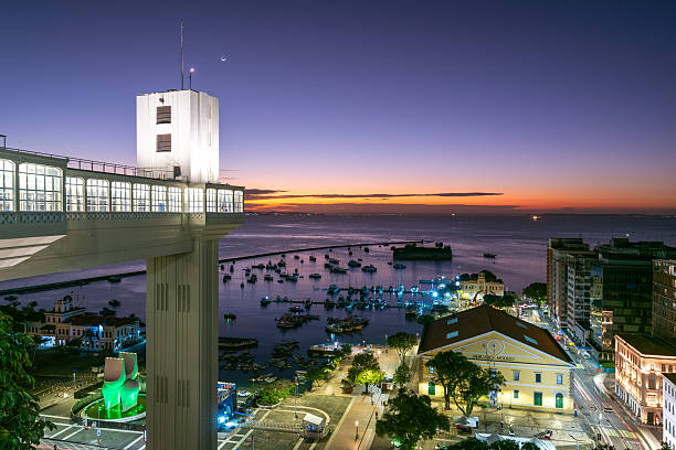 Salvador, Bahia - July 26, 2025: Famous Lacerda elevator illuminated at night with All Saints bay in the horizon with boats floating.