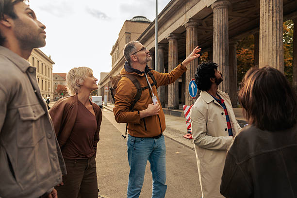 A guide points to Kolonnadenhof and shares information with a multicultural group of tourists during a city tour in Berlin. The group stands outdoors, appreciating architecture, history, and cultural exploration.