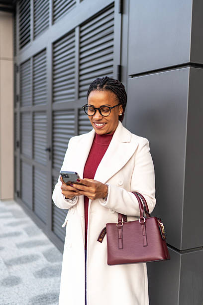 istock Smiling businesswoman checking phone while standing outdoors 2245326149