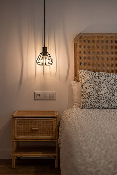 istock A cozy bedroom scene featuring a bed with a patterned white duvet and a rattan headboard. A bedside table holds a stylish pendant lamp, creating a warm ambiance. 2245327795