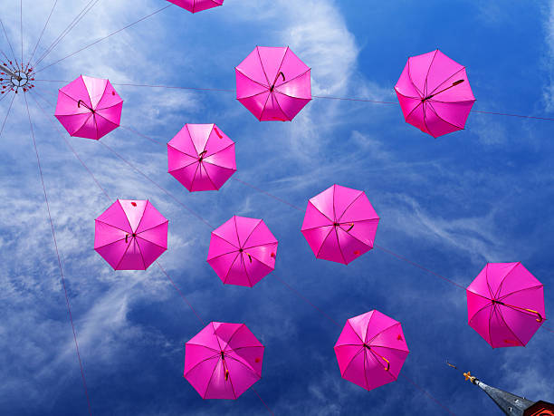 La Rochelle, France - Oct 02 2025: Fuchsia umbrellas suspended above a blue sky during Breast Cancer Awareness Month in La Rochelle, France, captured from below with a bright, uplifting mood.