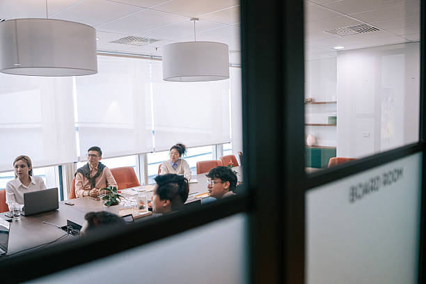 istock Asian Team Meeting Viewed Through Glass Wall in Modern Office Boardroom 2245334971