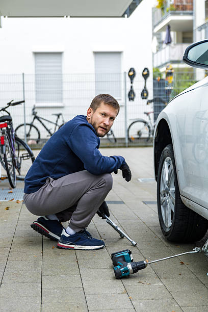 istock Man changing car tire using electric drill and jack on city sidewalk. DIY auto repair, maintenance, seasonal tire change, mechanical work, vehicle service, urban life. 2245335832