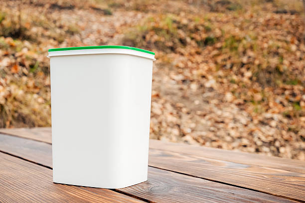 a white rectangular plastic container with a green lid standing on a wooden table in an autumn forest