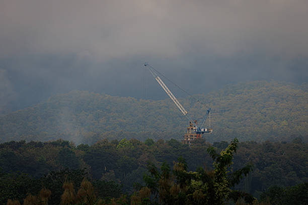 Industrial Marvel Above The Clouds: A towering crane pierces the misty atmosphere above a dense forest, symbolizing progress, industry, and the fusion of human endeavor with nature.