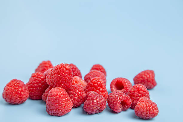 istock Simple arrangement of red raspberries on a light blue backdrop with empty space 2245343245