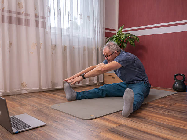 istock Senior man stretching while sitting on yoga mat during home exercise routine 2245345338