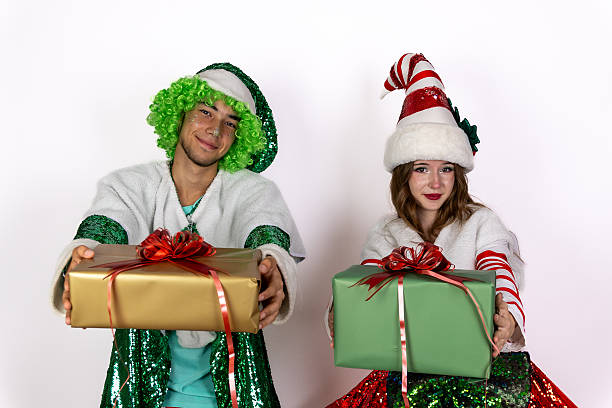 people dressed as elves holding Christmas presents, smiling joyfully amid a festive scene.