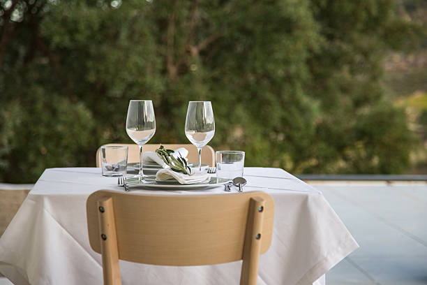 istock Table set for two outside, decorated with olive branches, white linens, and glassware. Surrounded by vineyards and mountains in rural Alijo, Portugal. Calm atmosphere, nature, rural tourism. 2245349917