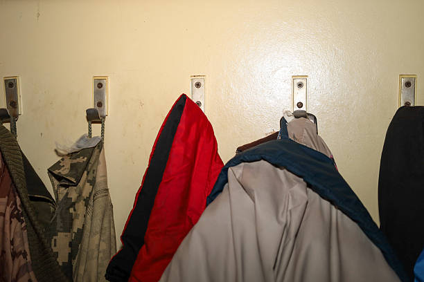 ​A row of metal hooks on a light wall, holding various outerwear, including a bright red jacket and camouflage uniform. The shot conveys the atmosphere of a changing room or hallway in a public or residential space.