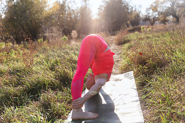 A person in pink athletic wear performs a deep backbend yoga pose on a mat in a sunlit prairie. Outdoor fitness, flexibility, balance, and calm energy evoke wellness and movement.