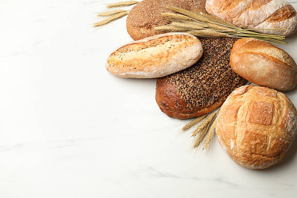istock Different types of bread and wheat spikes on white marble table, flat lay. Space for text 2245363057