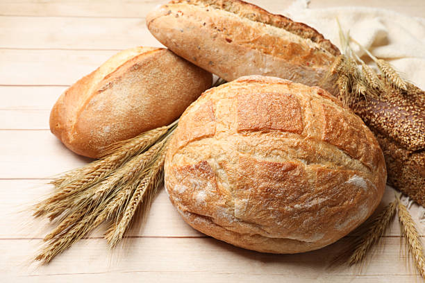 istock Different types of bread and wheat spikes on wooden table, closeup 2245363060