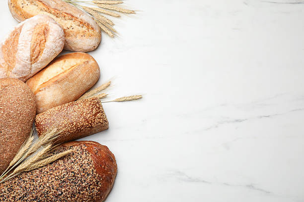 istock Different types of bread and wheat spikes on white marble table, flat lay. Space for text 2245365604