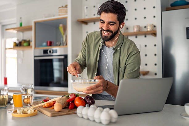 istock Smiling man mixing ingredients in modern kitchen with laptop fresh vegetables and coffee cup 2245369183