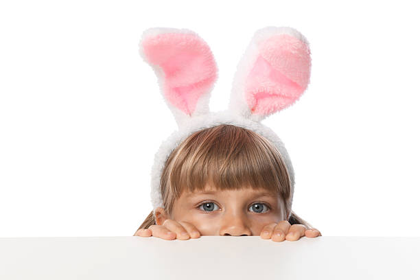 Curious little girl in bunny ears peeking over table against white background