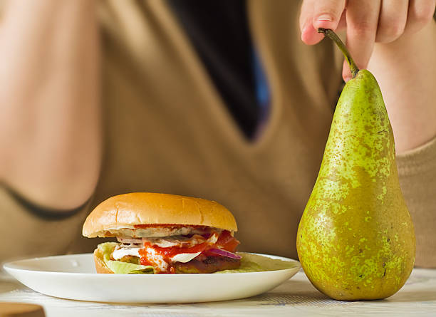 A still life of a healthy and unhealthy choice: a hamburger on one plate and a fresh pear on another