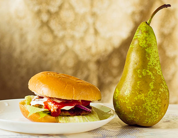 hamburger and a fresh pear on a table, symbolizing a food choice - Healthy or Junk Food: A fresh pear sits next to a juicy burger deity concept