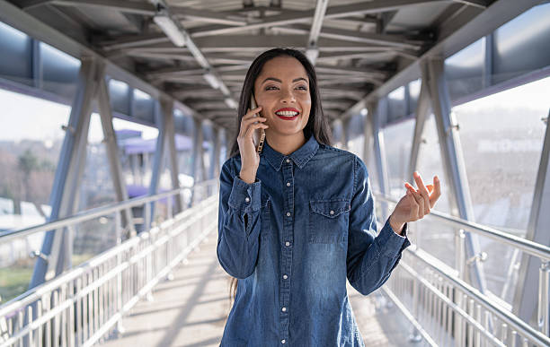 Young woman confidently chatting on her phone while walking along a modern urban bridge.