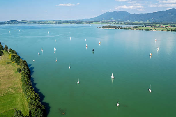 Aerial view of a summer landscape with a lake, sailboats, and mountains in the background under blue sky on a sunny day.