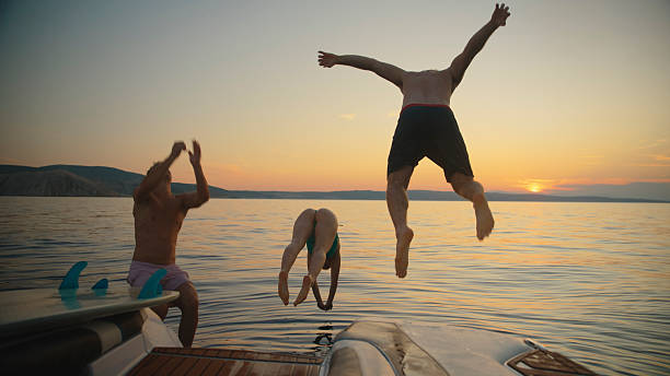 istock Young Friends Leaping Into Water From Boat at Sunset 2245377386