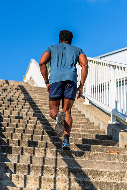 Fit African-American athlete in sportswear trains by running up concrete stairs on a sunny day, focusing on strength and endurance.