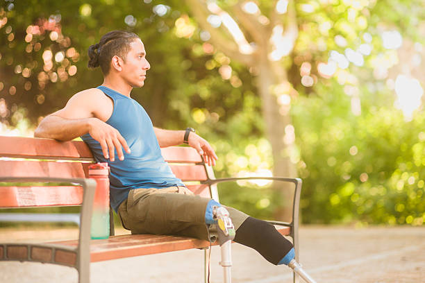 Man with prosthetic legs sitting on a park bench, taking a break from training in an outdoor setting