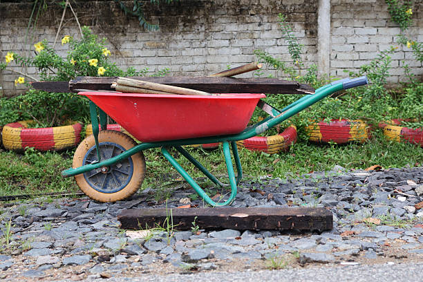 Old rusty red wheelbarrow beside a wall on a sunny day.