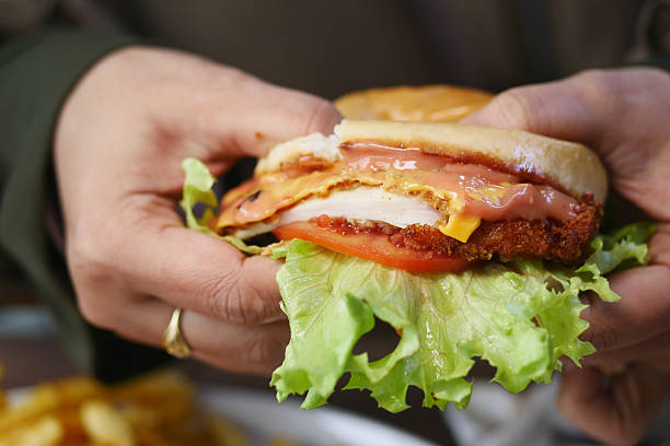 Hand holding a savory chicken sandwich with lettuce, tomato, and cheese.