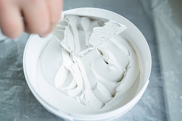 istock Hand using a spatula to mix smooth white paint in a round container, showcasing the texture and consistency of the material for artistic or renovation projects 2245382196