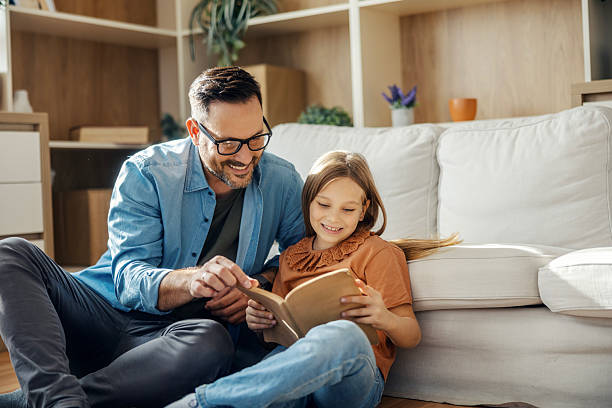 istock Father and daughter reading book together at home 2245391182