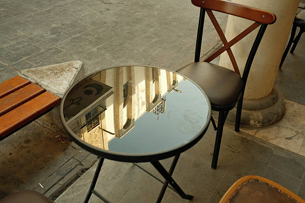 A round glass table reflecting buildings and a chair in an outdoor cafe setting