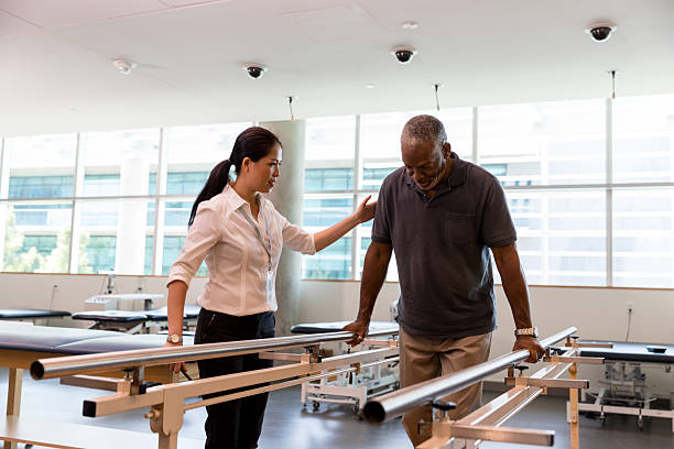 istock Physical therapist assists senior man using parallel bars during rehabilitation exercise. 2245398351