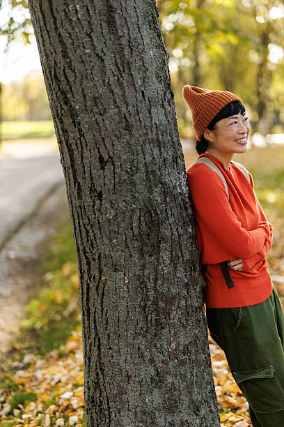 Portrait of beautiful Japanese woman leaning on tree and enjoying sunny autumn day in nature