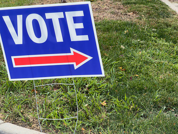 Blue yard sign displaying VOTE with a red arrow pointing right