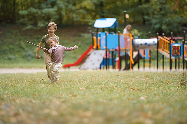 Children playing and running on grass with a stick at the public playground.