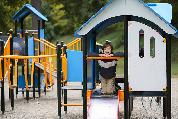 Young boy smiling at camera while playing on a colorful playground slide.