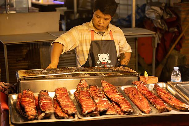 04 November 2025, Ko Samui - Thailand.Thai man stands behind her stall, preparing an order at a night market in Koh Samui. Men are essential to night markets, often managing food stalls, interacting with customers, and contributing significantly to the local economy.