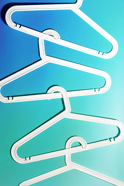 White Plastic hangers as abstract minimal pattern on soft gradient background of teal and blue color, Clothes rack for organizing clothes in closets or retail stores for hanging of garments, top view