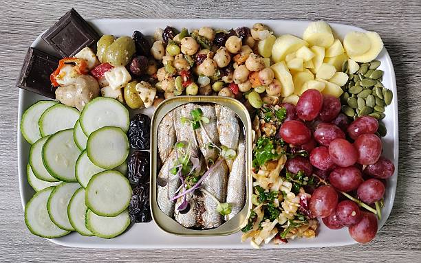 Delicious fresh food, including zucchini, Ajwa dates, sardines, red grapes, pumpkin seeds, white carrot, garbanzo bean salad, olive mix, dark chocolate